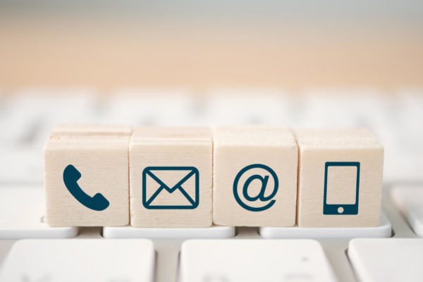 a phone, email, '@' symbol and phone icon on blocks on top of a keyboard.